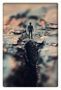 A lone figure stands at the edge of a deep crevasse, symbolizing the confrontation of life’s challenges or inner turmoil.